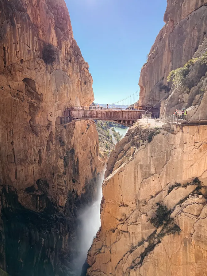 original bridge crossing the gaitanes gorge at el caminito del rey in malaga, spain. the new suspended bridge above the old bridge with the waterfall underneath it. hikers crossing the bridge